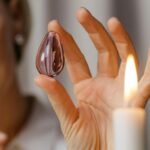 A woman gracefully holding an amethyst stone near a lit candle, embodying tranquility and elegance.